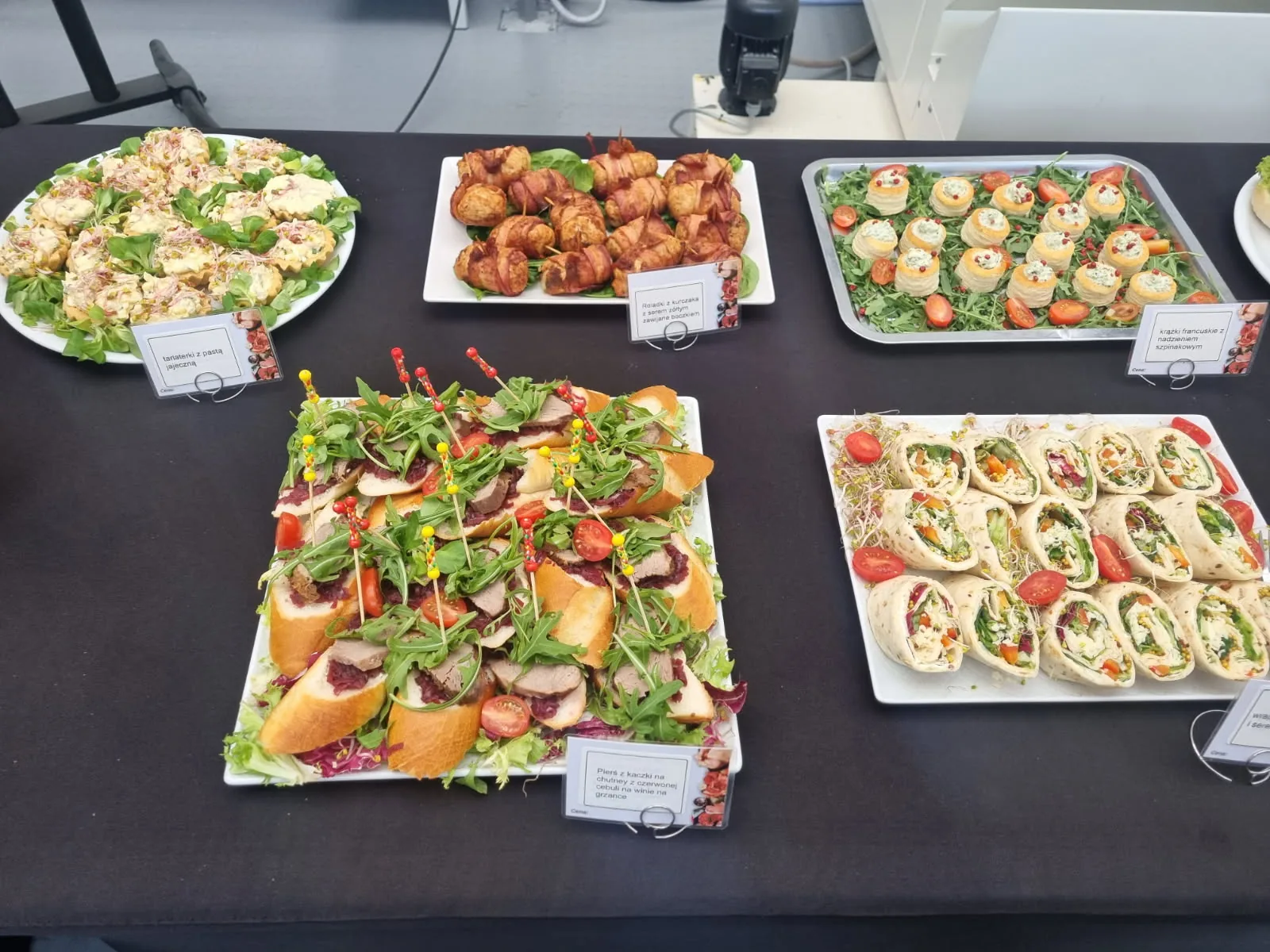 Catering na czarnym stole: tortille, sałatki, klopsiki i kanapki